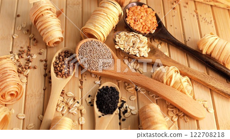 Wooden spoons with chia seeds, lentils, oats, and almonds, arranged on natural wooden surface, showcasing eco-conscious choices for healthy recipes using sustainable ingredients. Eco wooden spoons 122708218