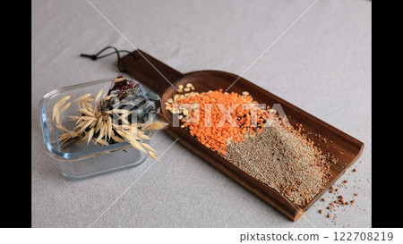 Wooden tray containing lentils, seeds, dried plants placed near bamboo coasters. Scattered grains create a minimalist, cozy atmosphere, emphasizing natural elements. Wooden tray containing lentils, seeds, dried plants placed near bamboo coasters. Scattered grains create a minimalist, cozy atmosphere, emphasizing natural elements. 122708219