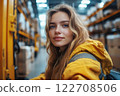 Woman operating forklift in warehouse aisle, surrounded by shelves stacked with packaged goods. 122708506