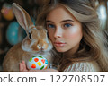 Teen girl holds Easter  rabbit and painted egg against blurred festive background. 122708507