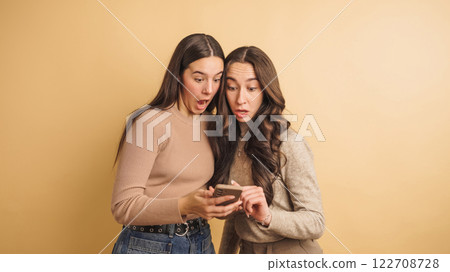Surprised friends sharing exciting news on smartphone Surprised friends sharing exciting news on smartphone 122708728
