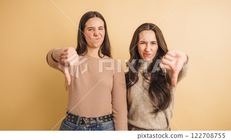 Young women showing thumbs down with disapproving expression on beige background 122708755
