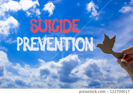 Suicide prevention symbol. Concept words Suicide prevention on beautiful blue sky. Psychologist hand, wooden bird. Beautiful blue sky background. Psychological suicide prevention concept Copy space Suicide prevention symbol. Concept words Suicide prevention on beautiful blue sky. Psychologist hand, wooden bird. Beautiful blue sky background. Psychological suicide prevention concept Copy space 122709017