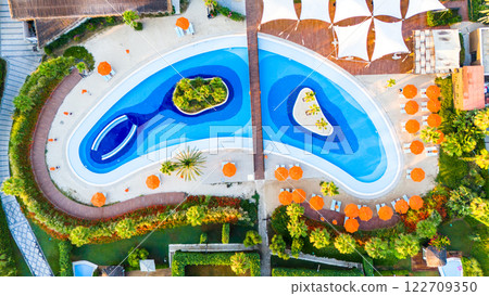 Aerial view of a luxury resort with a uniquely designed wave-shaped pool and sunbathing areas 122709350
