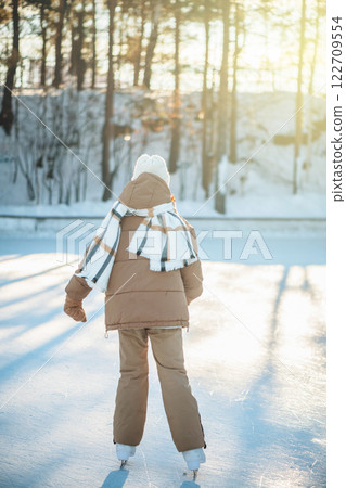 Adorable girl wearing warm winter clothes joyfully ice skating on a sunny winter day in a snowy park, embracing outdoor activities and relishing carefree moments of fun 122709554
