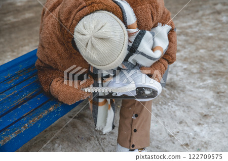 A girl puts protective covers on her ice skates, ensuring the blades stay sharp and protected while off the ice, promoting safe skating practices 122709575
