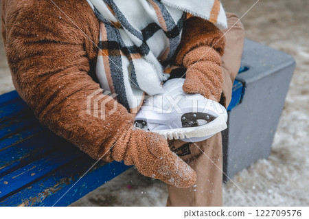 A girl puts protective covers on her ice skates, ensuring the blades stay sharp and protected while off the ice, promoting safe skating practices 122709576