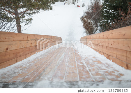 Wooden slide structure featuring snowy planks gliding down into a winter park, creating an exciting spot for children and families to enjoy sliding and playing in the snow 122709585