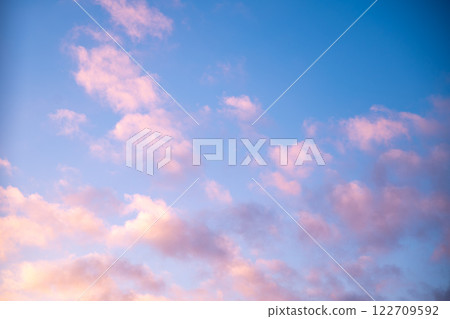 Scattered pink clouds drifting across a vibrant blue sky create a stunning sunset scene, radiating tranquility and warmth while inviting a sense of peacefulness and serenity 122709592