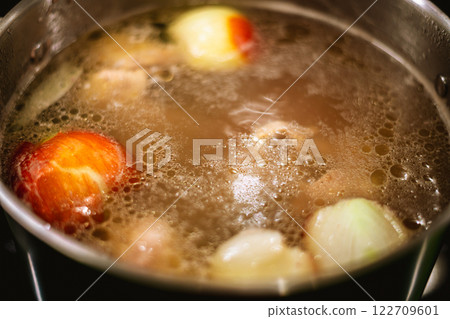 Simmering chicken broth fills the pot on the stove, combining tender pieces of chicken, fragrant onion, creating a rich and comforting stock full of flavor 122709601