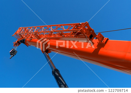 Construction crane arm with hook against blue sky background. Mobile construction tower crane with telescopic boom 122709714