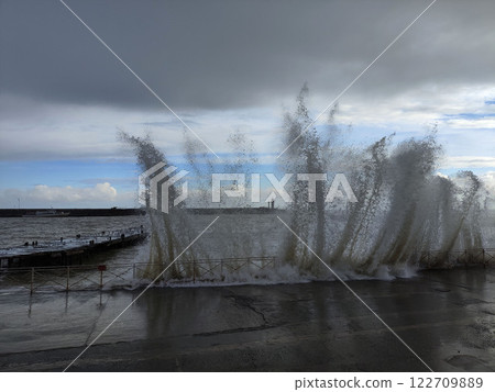 Waves crash against the shore creating splashes near a coastal walkway during a cloudy day 122709889