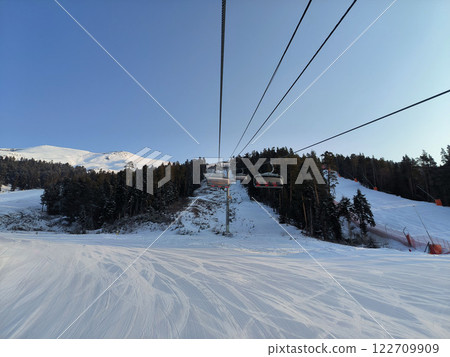 Scenic ski lift journey over snow-covered slopes and trees during a clear winter day in a mountainous region 122709909