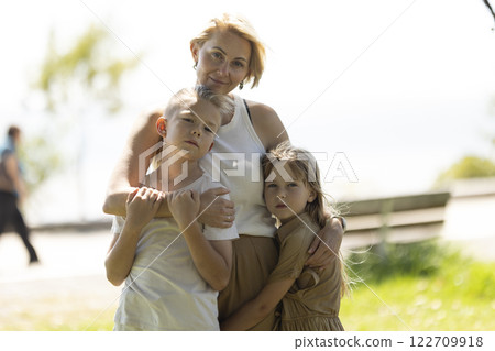 Loving mother embracing her two children outdoors Loving mother embracing her two children outdoors 122709918