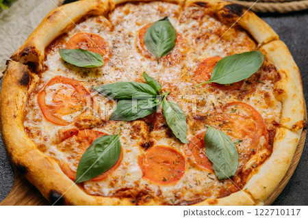 Classic Margherita pizza with fresh basil, tomatoes, and mozzarella on a wooden board 122710117