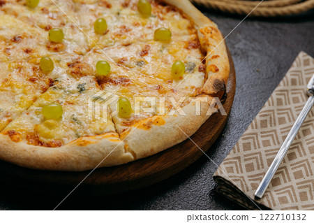 Gourmet four-cheese pizza with green grapes, served on wooden board in a stylish restaurant setting Gourmet four-cheese pizza with green grapes, served on wooden board in a stylish restaurant setting 122710132