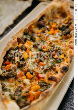 Turkish pide with minced meat, vegetables and cheese on a plate in a stylish restaurant setting 122710133