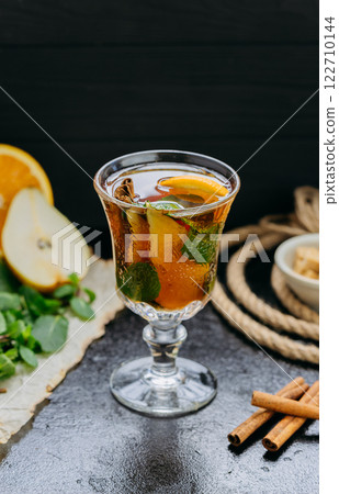 Aromatic herbal tea with citrus, cinnamon, and mint in a glass, set on a dark rustic background 122710144
