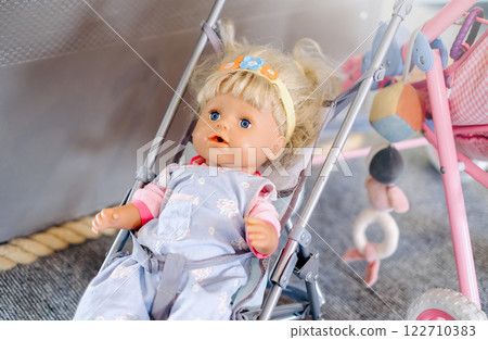 A doll is sitting in a stroller. The doll is wearing a yellow headband A doll is sitting in a stroller. The doll is wearing a yellow headband 122710383