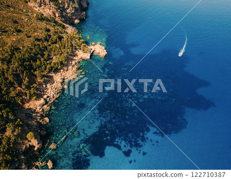 Aerial view of a rocky coastline with lush green vegetation and crystal-clear blue sea Aerial view of a rocky coastline with lush green vegetation and crystal-clear blue sea 122710387