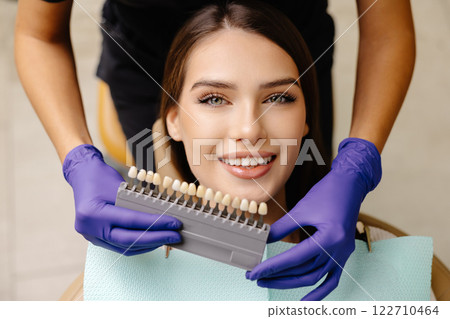 Dentist choosing teeth enamel shade color for young smiling female patient before whitening procedure Dentist choosing teeth enamel shade color for young smiling female patient before whitening procedure 122710464