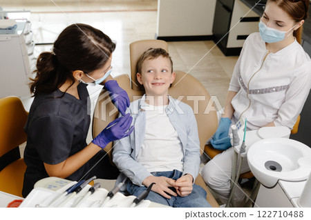 Kid in dental office. Dentist doing hygienic teeth cleaning to a boy sitting in a chair 122710488