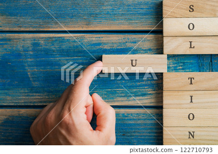 Male hand pushing a wooden peg into a stack of them to spell the word Solution 122710793