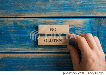Male hand assembling a No gluten sign written over two wooden pegs Male hand assembling a No gluten sign written over two wooden pegs 122710794