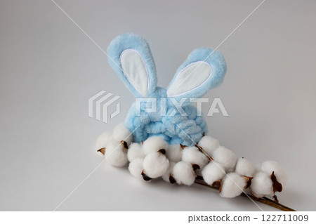 White cotton flowers and a blue headband with rabbit ears on a white background. The concept of Easter. a place for your text. 122711009