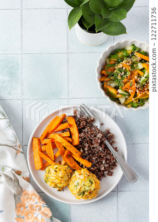 A healthy and filling meal of brown rice, baked sweet potato and squash chickpea pancakes, packed with flavor and nutrients, fresh salad of tomatoes and cucumbers 122711736