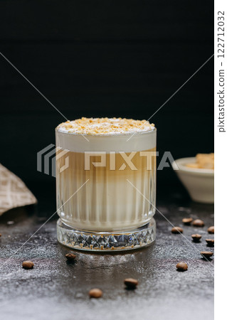 Layered latte with frothy milk and crushed nuts in crystal glass with coffee beans on dark table Layered latte with frothy milk and crushed nuts in crystal glass with coffee beans on dark table 122712032
