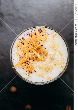 Gourmet layered latte with whipped foam, orange zest, and spices, served on a rustic dark surface 122712083