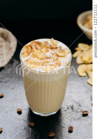 Creamy latte with whipped foam, dried apple slices, and cinnamon, served on a dark textured surface 122712111