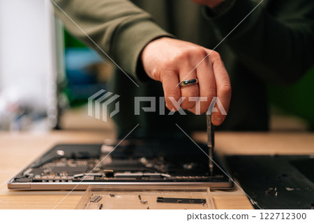 Close-up hands of unrecognizable computer master using screwdriver to repair motherboard of disassembled laptop in workshop. Concept of process electronic device repair. Close-up hands of unrecognizable computer master using screwdriver to repair motherboard of disassembled laptop in workshop. Concept of process electronic device repair. 122712300