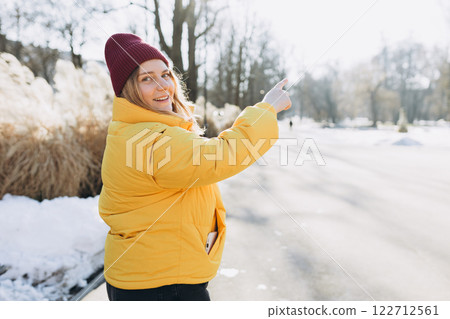Happy blonde 30s woman walking outdoors on street in city, pointing to something. Winter time. Charming female wearing stylish outfit. Urban lifestyle concept. Happy blonde 30s woman walking outdoors on street in city, pointing to something. Winter time. Charming female wearing stylish outfit. Urban lifestyle concept. 122712561