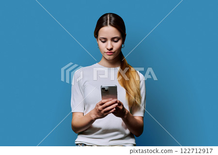 Young beautiful woman using smartphone on blue studio background 122712917