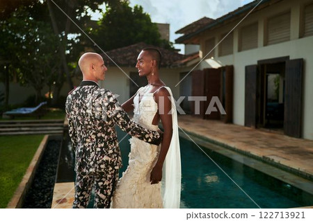 Ambiguous gender fluid black bride in white dress and LGBTQ groom in bold suit marry at tropical villa. Wedding venue for gay-friendly event. Celebrating diversity, love, union. 122713921