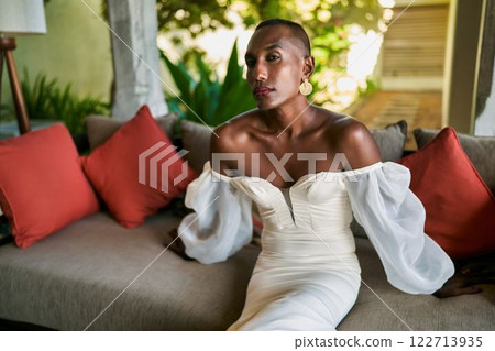 Ambiguous person in elegant white dress sitting at villa. Gender fluid bride on couch, trees in background. Unique LGBTQ wedding theme. Fashionable, stylish, diverse, inclusive imagery. Ambiguous person in elegant white dress sitting at villa. Gender fluid bride on couch, trees in background. Unique LGBTQ wedding theme. Fashionable, stylish, diverse, inclusive imagery. 122713935