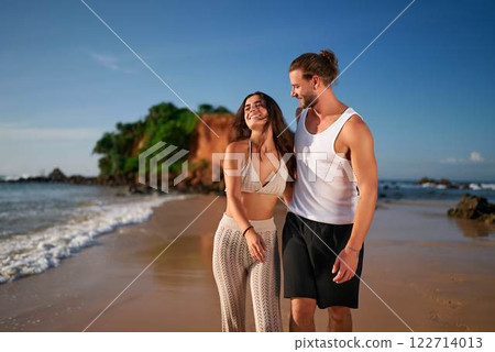 Affectionate adult couple stroll sandy beach at sunrise. Romantic duo walk near sea, childfree getaway. Laughing man, woman enjoy vacation, leisure stroll. Travel, summer, love, coast experience. 122714013