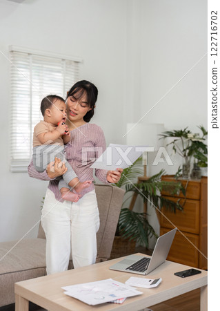 Mother holding her baby while reviewing important documents at home. 122716702