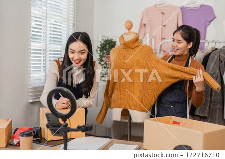 Two diverse retail workers showcasing a sweater while managing inventory and recording content. 122716710