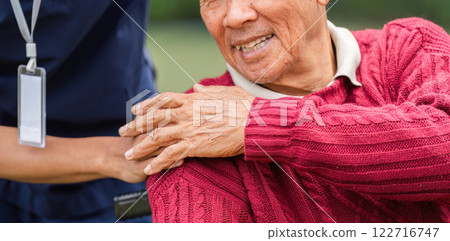 Close-up of elderly man's joyful smile with caregiver's hand providing gentle support in the garden 122716747