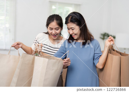 Excited daughter and mother exploring their shopping bags together, sharing a joyful moment 122716866
