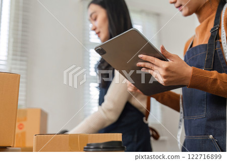 Two diverse warehouse workers organizing packages and managing inventory with a tablet. 122716899