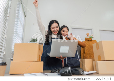 Two diverse retail workers expressing excitement and celebration while using a laptop. Two diverse retail workers expressing excitement and celebration while using a laptop. 122716921
