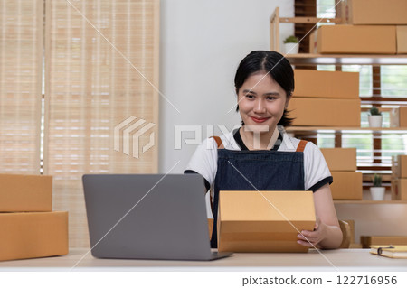 young female entrepreneur writes on the front of a product box to sell products online and prepares to send them to customers. Online selling at home, working from home young female entrepreneur writes on the front of a product box to sell products online and prepares to send them to customers. Online selling at home, working from home 122716956