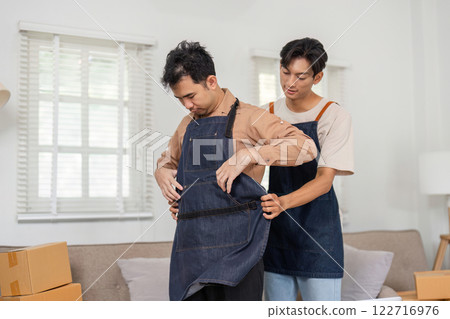 LGBT couple sharing warm moments while dressing in aprons, supporting each other at home LGBT couple sharing warm moments while dressing in aprons, supporting each other at home 122716976