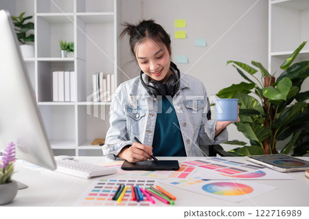 Female designer wearing headphones listening to music while doing graphic design work Choose colors for working with the computer at the table. 122716989