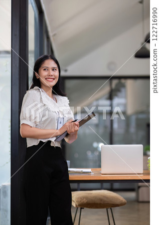 Confident businesswoman standing with clipboard in a stylish modern office 122716990