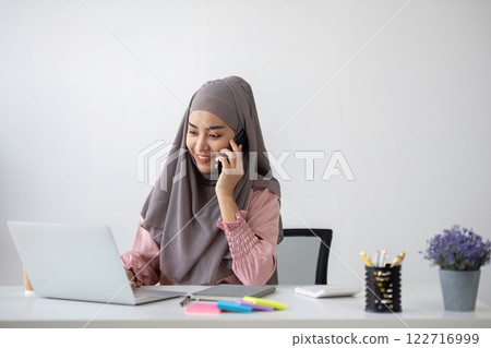 Smiling Muslim business woman Wearing a hijab while chatting online on a work desk in the office. 122716999